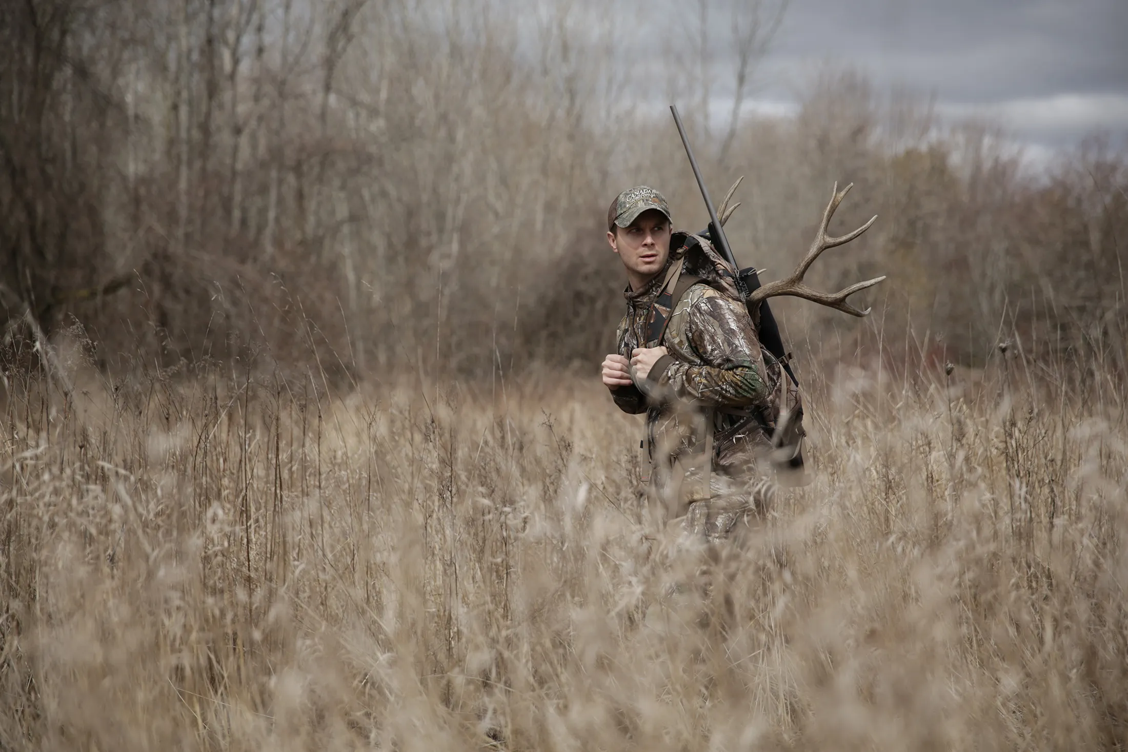 Hunter in camouflage carrying antlers through tall autumn grass